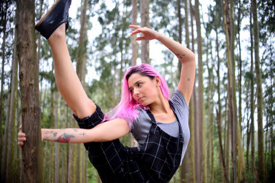 Young woman exercising while standing by tree trunk in forest