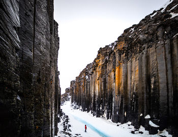 Unrecognizable traveler walking in between spectacular scenery of rocky ravine with frozen river in highlands in iceland