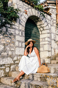 Attractive young woman in white dress sitting on stairs in old town. lifestyle, summer.