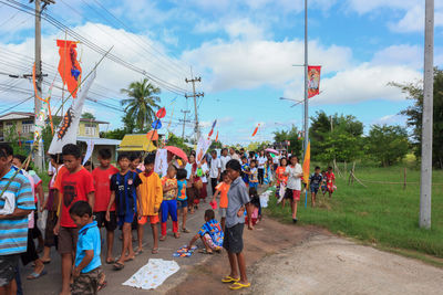 People on street amidst trees in city against sky