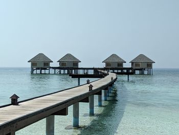 Stilt houses on pier by sea against clear sky