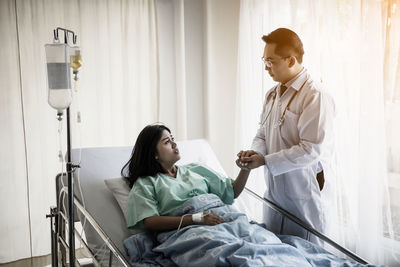 Doctor consoling patient lying on bed at hospital