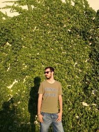 Young man wearing sunglasses standing against creeper plants