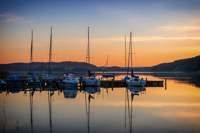 Sailboats moored at harbor against sky during sunset