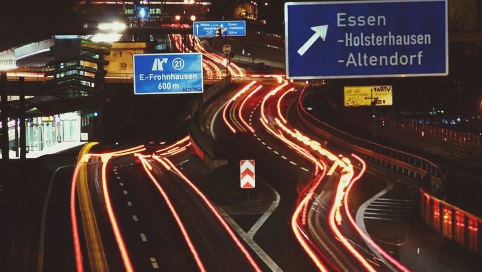 illuminated, night, text, transportation, western script, communication, long exposure, light trail, speed, road, city, motion, traffic, street, guidance, sign, information sign, red, high angle view, arrow symbol