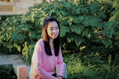 Portrait of young woman standing against plants