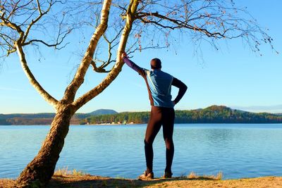 Silhouette of sport active adult man in running leggins and blue shirt at birch tree on beach. 