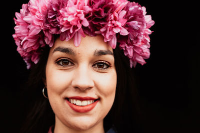 Close-up portrait of smiling young woman against black background