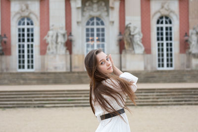 Portrait of smiling young woman standing against built structure