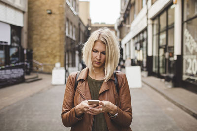 Young woman using mobile phone on road in city