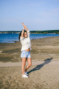 Young woman with arms raised standing on sand against sea at beach