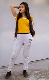 Young woman looking away while standing against wall