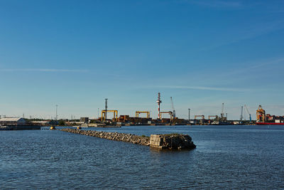 Factory by sea against blue sky