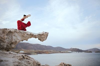 Man on rock by sea against sky