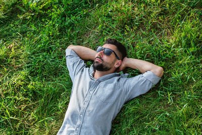 Young handsome sports european man in sunglasses is resting on a grass in summer park, top view.