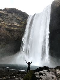 Man standing on rock against waterfall