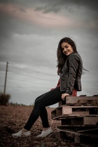 Portrait of woman sitting on crates against sky