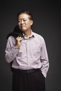 Senior businessman with hand in pocket while standing against black background