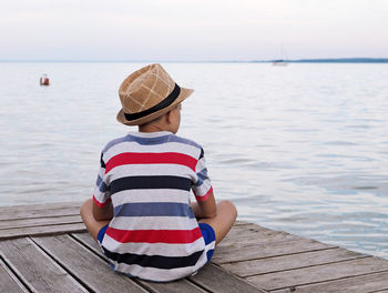 Rear view of man sitting on pier over sea