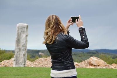 Rear view of woman photographing through camera while standing on field