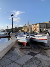 Boats moored on street by buildings against sky