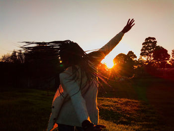 Rear view of woman standing on field against sky during sunset