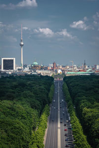 Highway amidst forest with fernsehturm berlin against cloudy sky