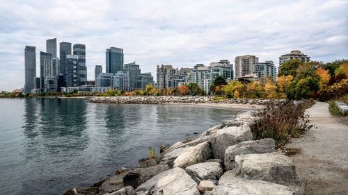 Buildings by river against cloudy sky during autumn