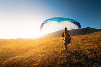 Rear view of woman walking on field against sky during sunset