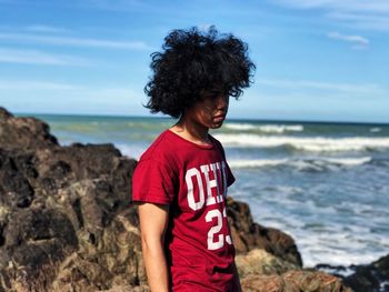 Young man standing by rocks against sea