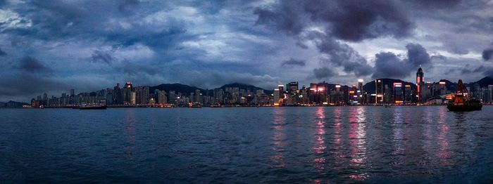 Panoramic view of illuminated buildings by sea against sky