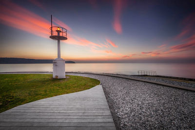 Footpath by sea against sky during sunset