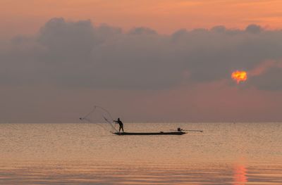 Silhouette man standing in sea against sky during sunset