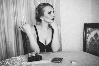 Thoughtful mid adult retro woman holding cigarette at dining table