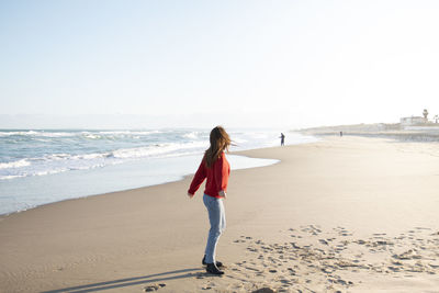 Rear view of woman standing on beach against sky