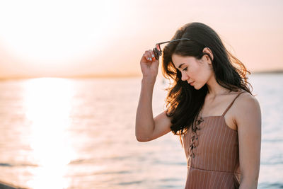 Young woman standing at beach during sunset