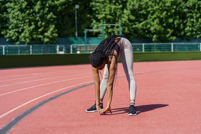 Fit african american woman enjoys stretching body standing on red track of city stadium near park