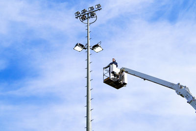 Low angle view of man standing in cherry picker against sky