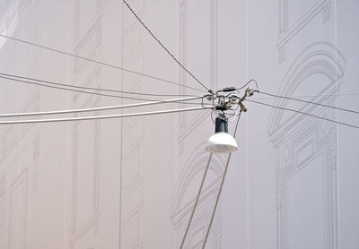 Low angle view of electrical lamp and cables against white wall 