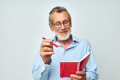 Smiling senior man holding notebook against white background