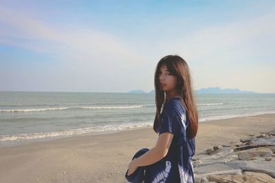 Side view portrait of young woman standing at beach against sky
