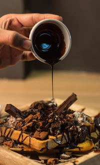 Close-up of hand pouring chocolate syrup on waffle