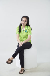 Portrait of smiling young woman sitting against wall