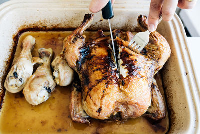 High angle view cropped hand cutting roasted chicken in tray