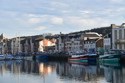 Sailboats moored on canal amidst buildings in city against sky