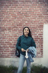 Smiling teenage girl with headphones against wall