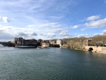 Buildings by river against sky in city