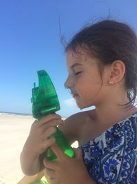 Close-up of girl spraying water with bottle at beach against clear blue sky