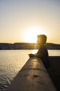 Man sitting on rock against sky during sunset