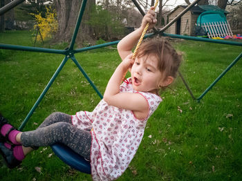 Full length of cute girl sitting on swing over grass field